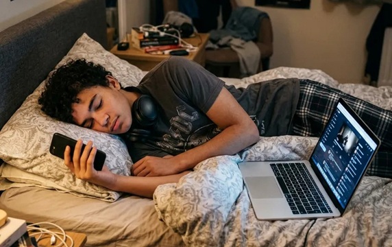 Teenage boy sleeping with laptop and phone
