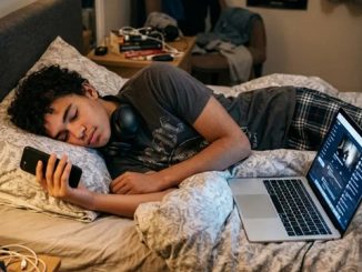 Teenage boy sleeping with laptop and phone